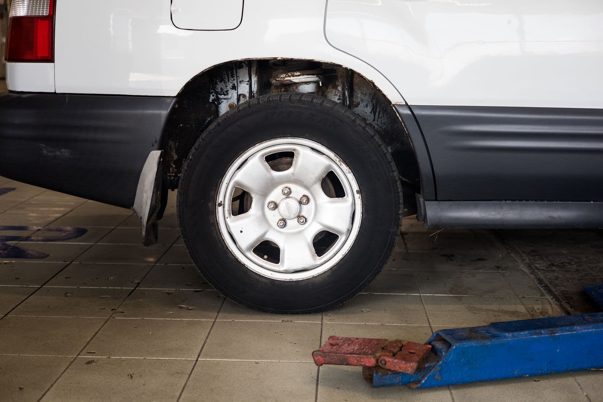 A white SUV raised on a trolley jack in a workshop bay