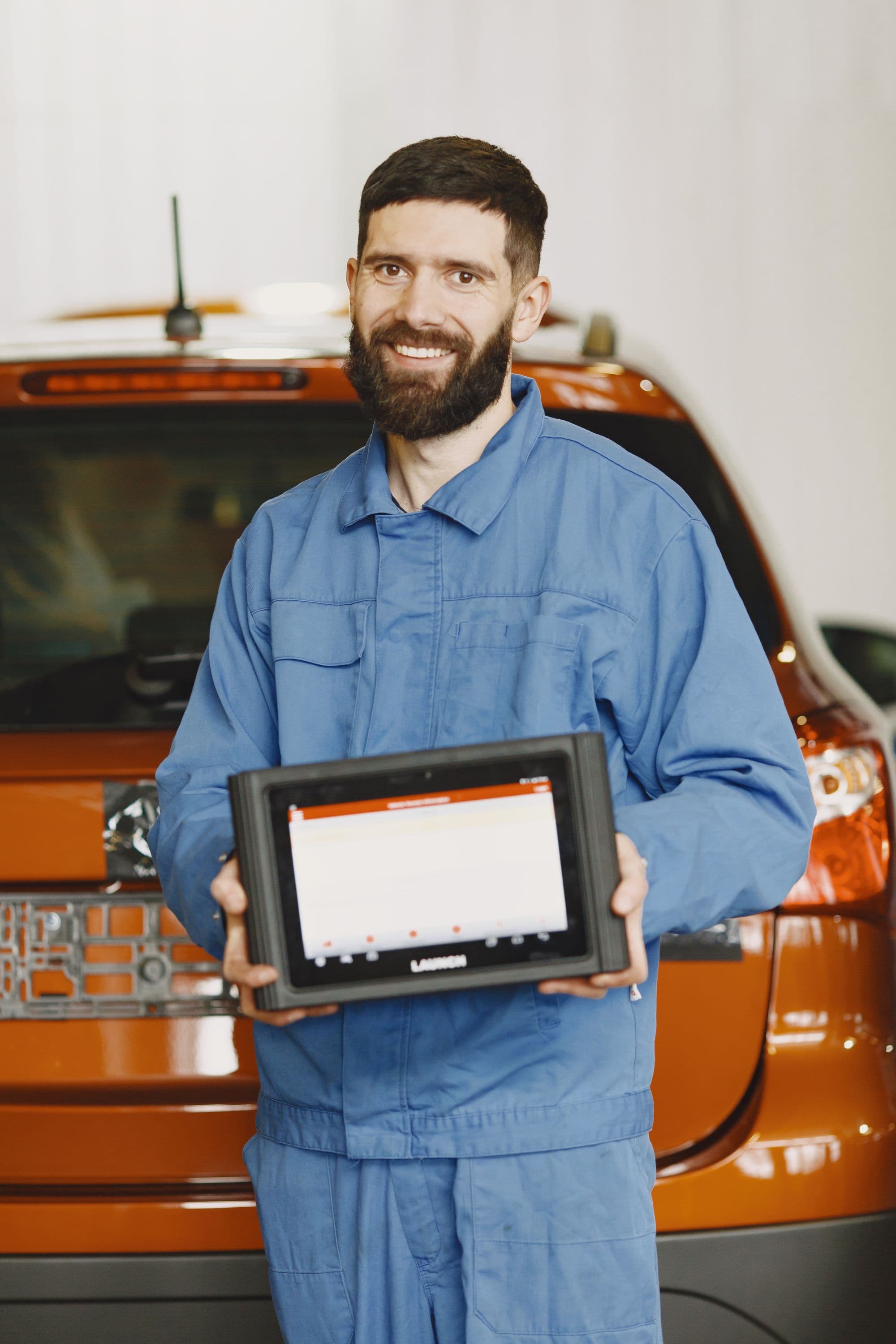 A mechanic holding a diagnostic tablet beside an orange car