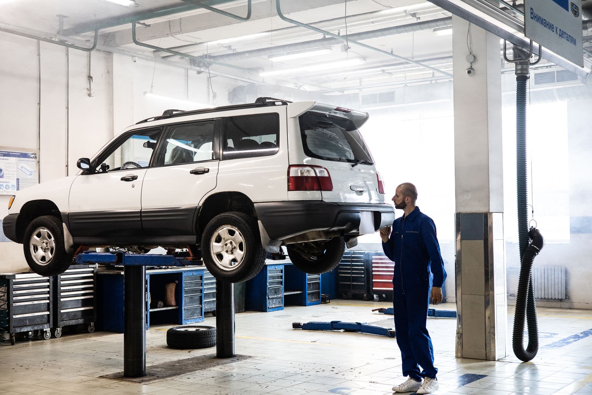 A mechanic inspecting a white SUV on a lift in a bright workshop