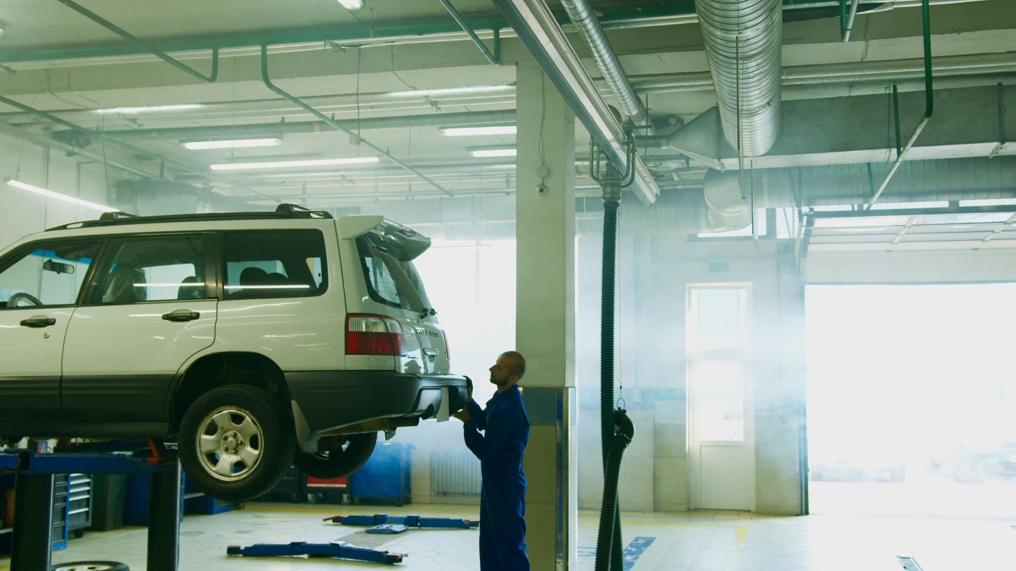 A mechanic at the rear of a car on a lift
