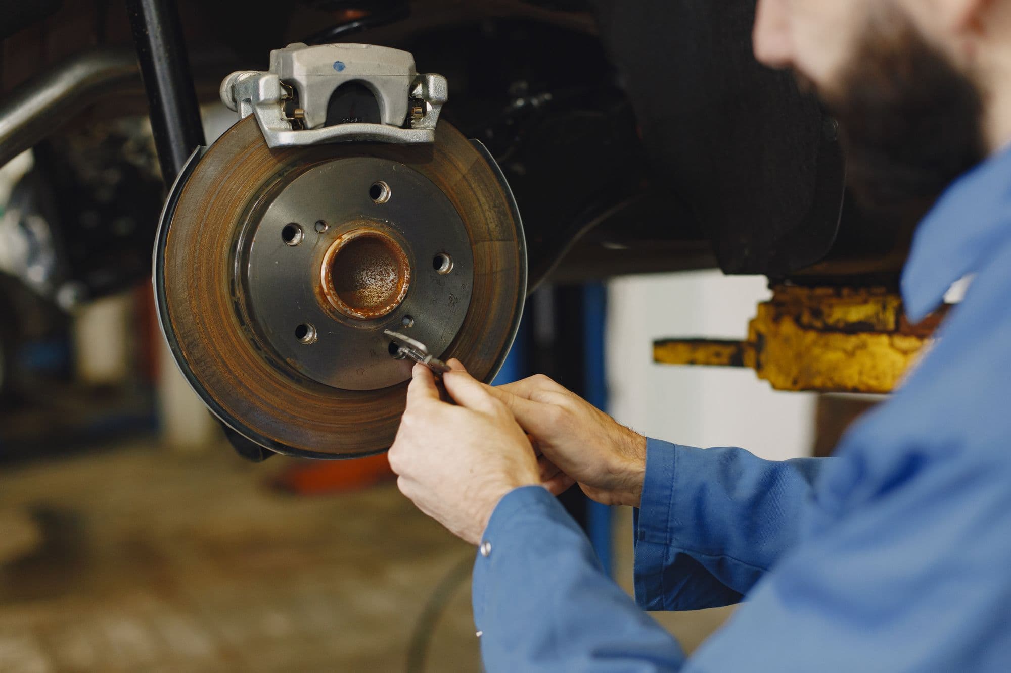 A mechanic checking a worn brake disc on a raised car